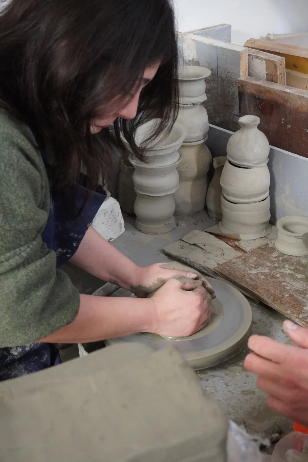 Frida's hands centring clay on the wheel, with pieces drying behind